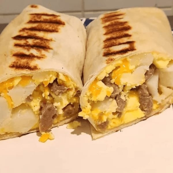 Two grilled breakfast burritos, cut in half, revealing eggs, cheese, sausage, and potatoes.