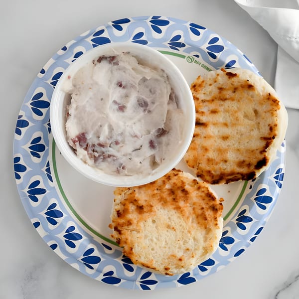 Toasted flatbreads and a container of white spread with dark specks on a blue and white paper plate.