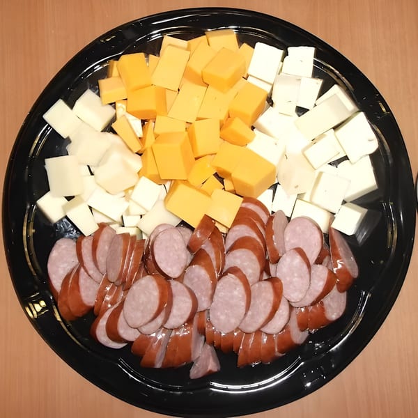 A black platter filled with cubed yellow and white cheeses, and sliced sausage.