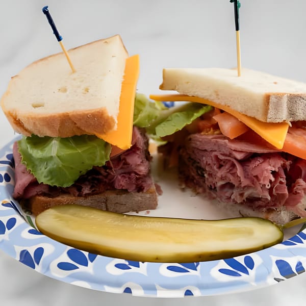 Two halves of a deli sandwich with meat, cheese, lettuce, and tomato, with a pickle spear.